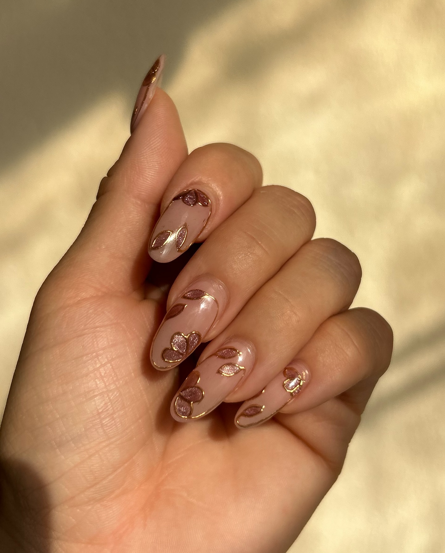 Nude almond nails with hand-drawn gold-outlined petals